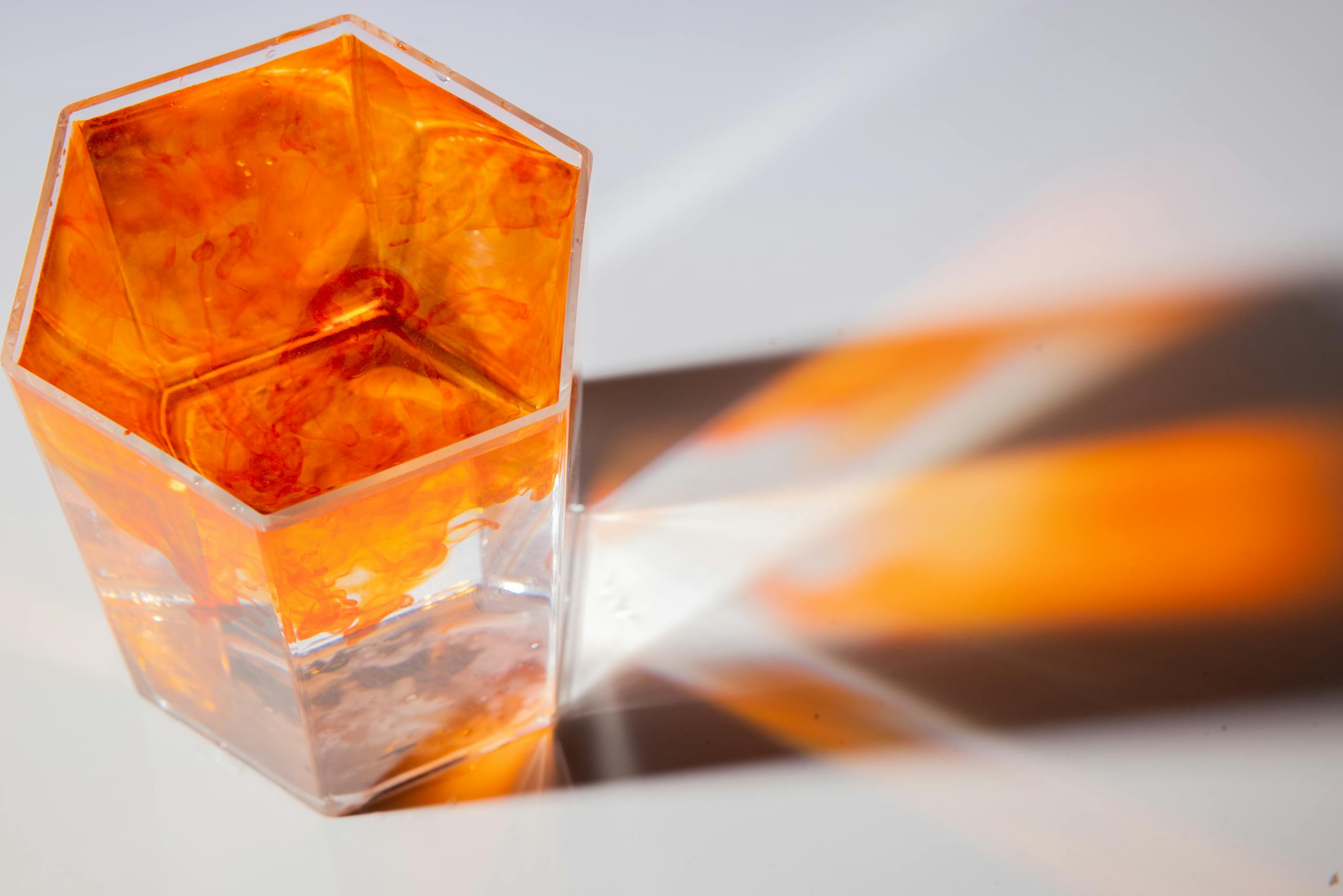 Orange dye in hexagonal glass creates vibrant flow and dynamic reflections on surface.