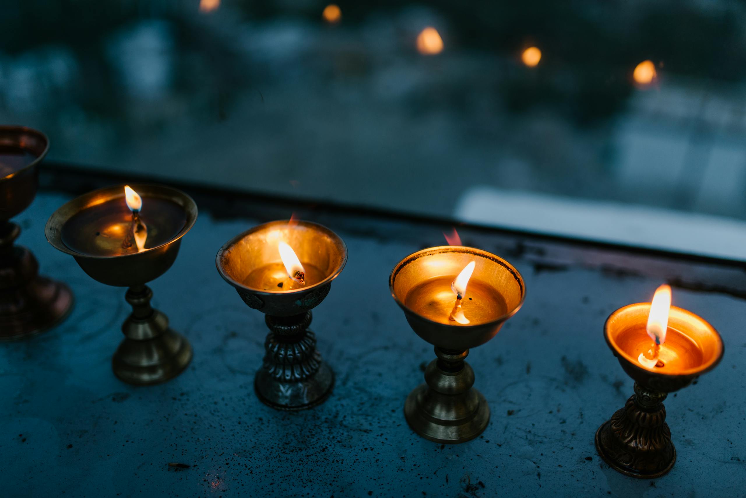 Elegant brass oil lamps lit with warm candle flames, reflecting ritual traditions.