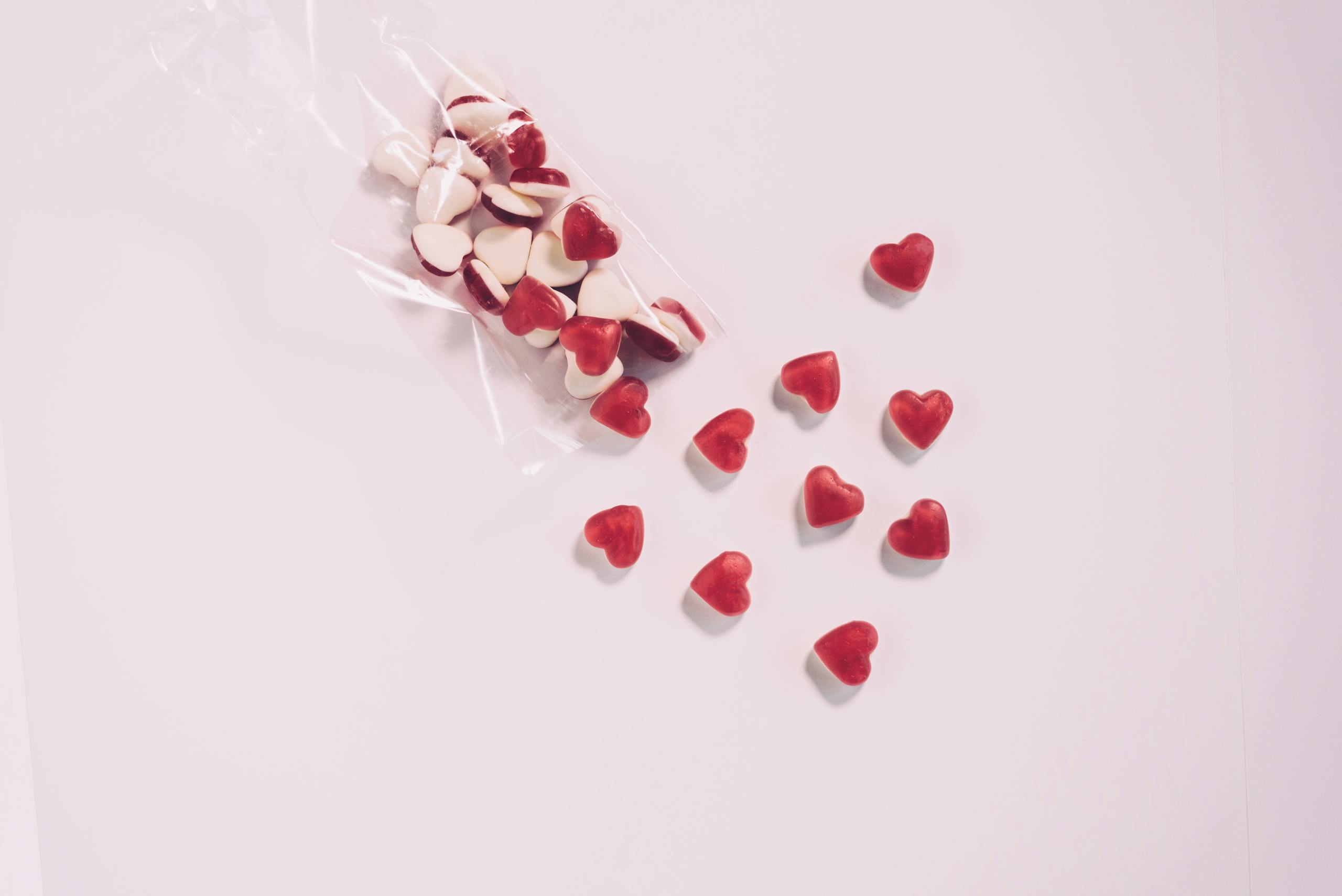 Scattered red and white heart candies on a minimalist background, evoking love and romance.